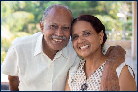 50717987 - closeup portrait, retired couple in white shirt and dress holding each other smiling,enjoying life together, isolated outside green trees background.